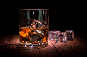 A glass of whisky and some ice cubes on the wooden table