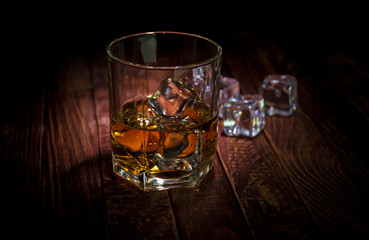 A glass of whisky and some ice cubes on the wooden table