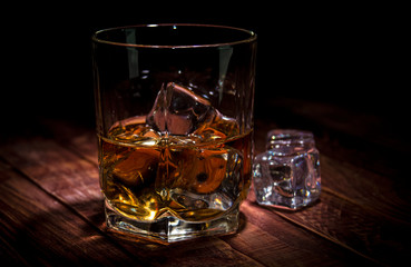 A glass of whisky and some ice cubes on the wooden table