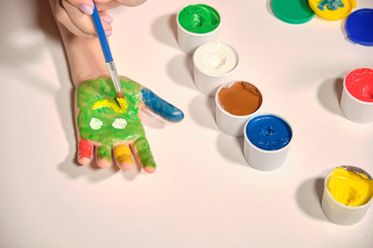 Little girl paints her hands with finger paint on white background