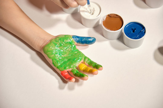 Little girl paints her hands with finger paint on white background