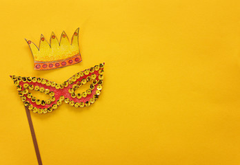 carnival party celebration concept with paper mask and crown over yellow background. Top view. Flat...