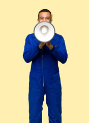 Young afro american worker man shouting through a megaphone to announce something on isolated background