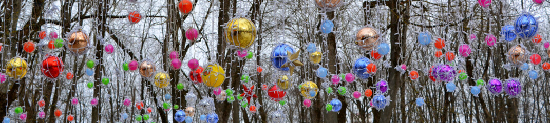 Multicolored balls and garlands among the snow-covered trees. Beautiful winter background.