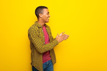 Young afro american man on yellow background applauding after presentation in a conference