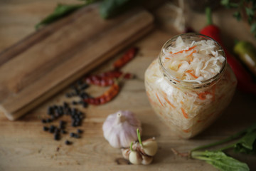 sauerkraut in a glass jar on a wooden table with spices and herbs with copy space for text. Top view.