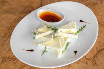 White cheese typical of the Balkans with arugula, dressing and, optionally, olive oil with red pepper. In a white plate on a wooden background.