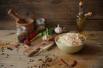 sauerkraut in a bowl on a wooden table with oil in a bottle, spices and herbs