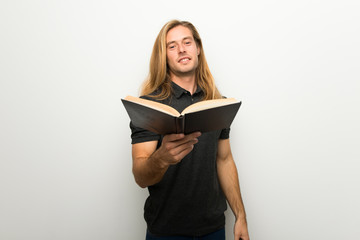 Blond man with long hair over white wall holding a book and giving it to someone