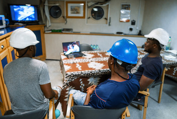 Seamen crew onboard a ship or vessel having fun watching movie on laptop. Recreation during at sea