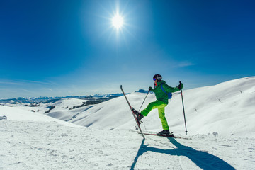 Fototapeta na wymiar Skier standing with one raised leg on a ski slope at a sunny day and looking somewhere
