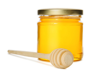 Glass jar full of sweet honey and wooden dipper isolated on white background. Focus on wooden dipper.