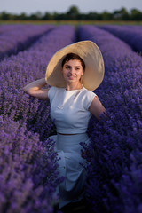 Close up of an elegant young woman in a white dress and a hat walking through a lavender field