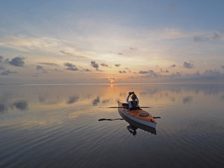 Fototapeta na wymiar Woman kayaking at sunrise on the perfectly still water of Bear Cut off Key Biscayne, Florida.