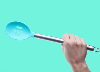 Hand holds silicone cooking spoon with metal handle. Isolated on blue background. Top view..