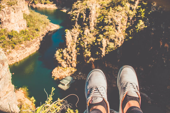 Feet of traveler sitting over chasm with mountain river canyon at background. View from the observation deck of Furnas Canyons. Capitolio, Minas Gerais, Brazil