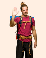 Hiker man with mountain backpacker saluting with hand with happy expression on isolated background