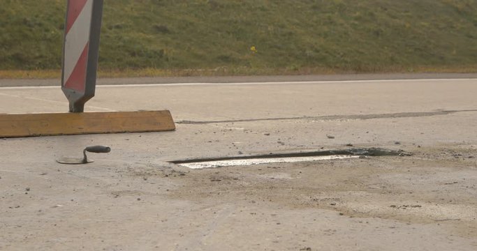 Close up of pit in asphalt road repaired with concrete patch at road construction site. Road works concept. Teamwork. Group of workers on a road construction. Team of people at work.