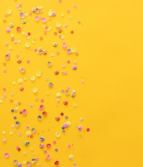 pastel colorful sequins on a yellow paper. Decorative accessories for sewing and party. Blank background with space for text