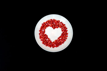 On a white plate from pomegranate seeds composite heart shape. Black background. Flat layer.