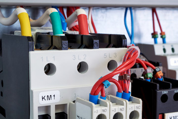 Electrical cables and wires are connected to electrical equipment. Front additional contacts are fixed on magnetic starters. Modern equipment in the electrical Cabinet. Color and digital marking.