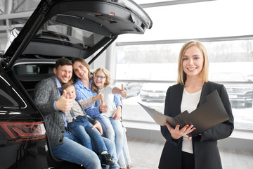 Car dealer posing at camera with family, buyers of new car.