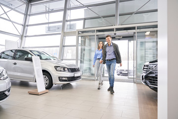 Fototapeta premium Couple entering dealership showroom, holding hands.