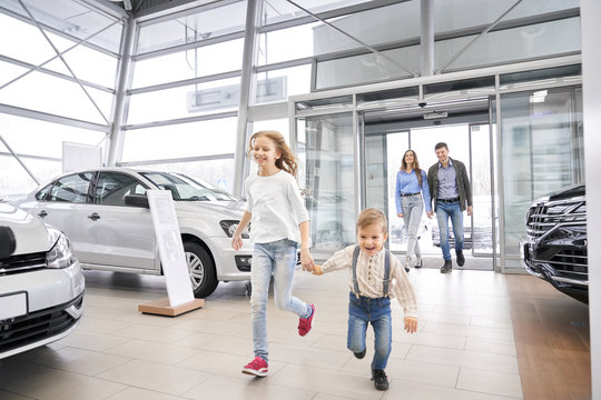 Family entering car dealership, happy children running.