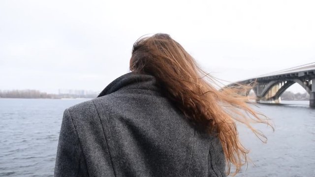 Portrait of a cute brunette girl near the river wind in the city.