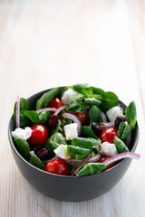 Winter salad with lamb's lettuce, spinach, cherry tomatoes, red onion, dried cranberries and goat cheese. Grey ceramic bowl, white wooden table, high resolution
