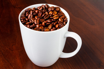 Roasted Coffee beans in a white mug cup isolated on a rustic wood table