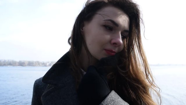 Young brunette girl in a coat near the river in the city.