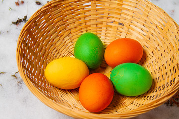 Five colorful easter eggs in a straw basket on top of snow and grass isolated egg hunt