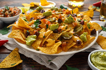 Mexican nachos tortilla chips with olives, jalapeno, guacamole, tomatoes salsa, cheese dipand beer.