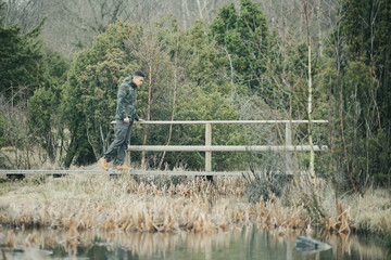 A young guy who hiking in a nature reserve in Sweden walks over a small bridge that goes over a...