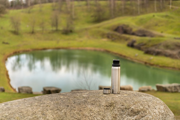 A coffee thermos on a cliff in a nature reserve in Sweden with a small lake down in a valley