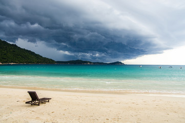 Fototapeta na wymiar Lonely chaise longue on a deserted beach, against a background of approaching tropical thunderstorm. Pulau Perhentian, Malaysia.