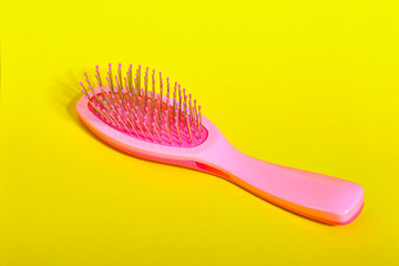 Pink comb from a handbag on a yellow background.