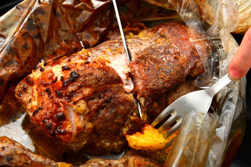 Roasted meat baked in the oven, knife and fork cutting roast.