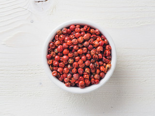 Pile with dried pink pepper berries on white wooden table. Close up view of pink peppercorn. Top view or flat-lay.
