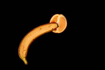 Banana and orange with a condom, safe sex concept, phallus and vagina on black background.
