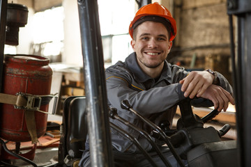 Portrait of metalworker wearing orange hardhat and gray protective suit smiling and looking at...