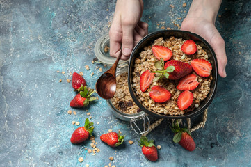 Healthy breakfast concept. Homemade granola with nuts and strawberries. Hands on shot. Morning light from the window.
