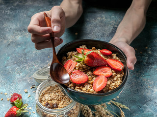 Healthy breakfast concept. Homemade granola with nuts and strawberries. Hands on shot. Morning light from the window.