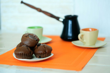 Chocolate muffins on the background of cups and coffee pots.