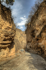 Rough dirt road turns into a paved road in a close canyon with bright blue sky