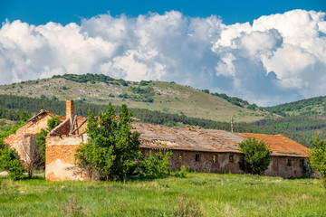 Abandoned agricultural buildings at the village of Rayanovtsi in Dragoman Municipality, Sofia Province, western Bulgaria, a karst mountain and beautiful cumulus clouds in the background
