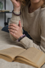 girl with quartz and amethyst bracelets holding a deer antler, a girl with a beautiful manicure holding a deer antler, books on background (vertically, close up).