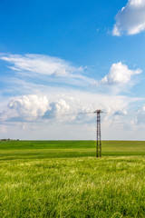 Fototapeta na wymiar Lonely electricity pylon in a Bulgarian spring field under a beautiful cloudy sky
