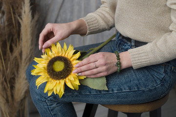 the girl has a jade bracelet, the girl is holding an artificial sunflower flower, the girl is sitting on a chair and holding a sunflower (horizontally).